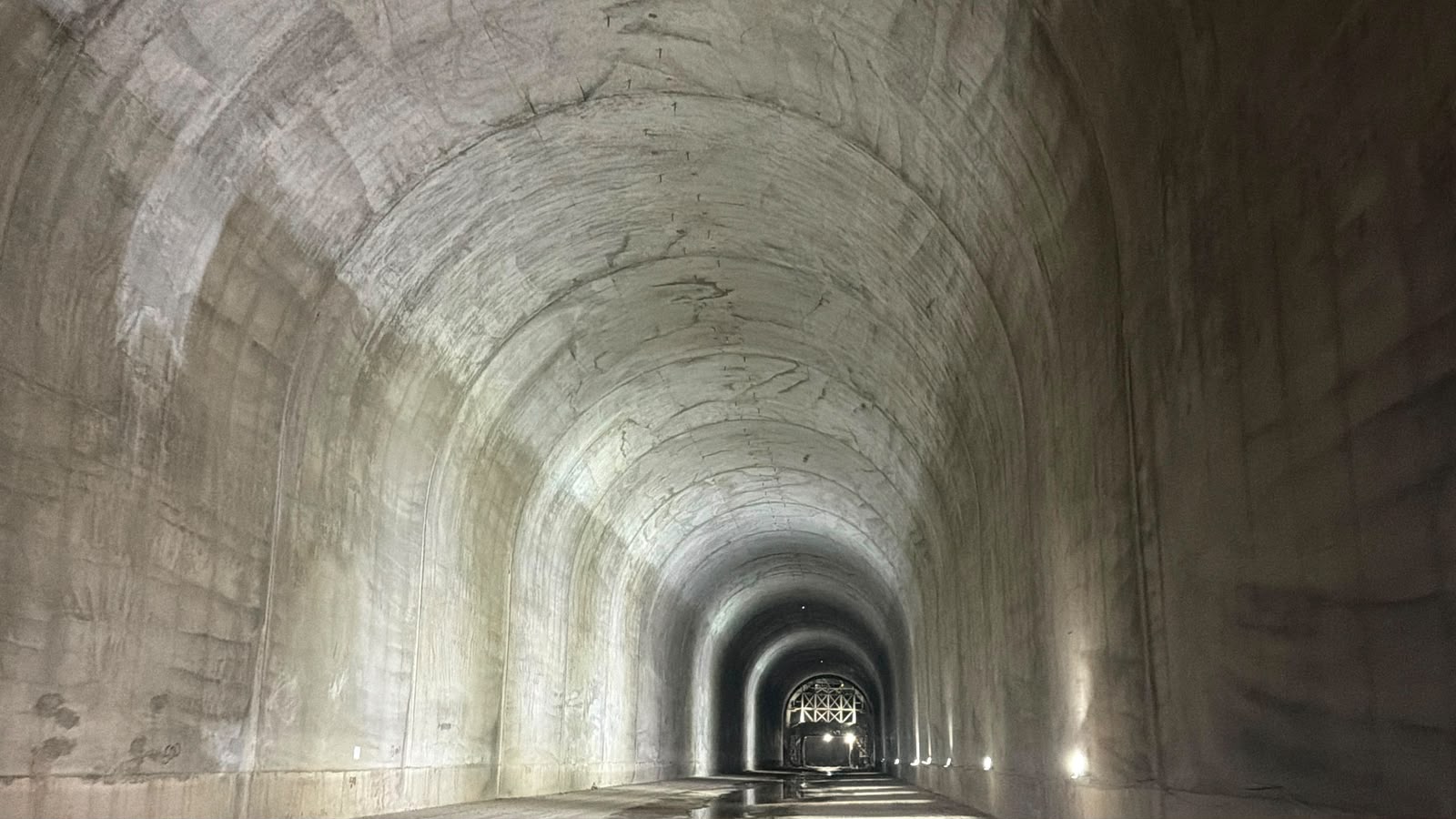 Concrete-lined tunnel bore curving away toward a lit gantry